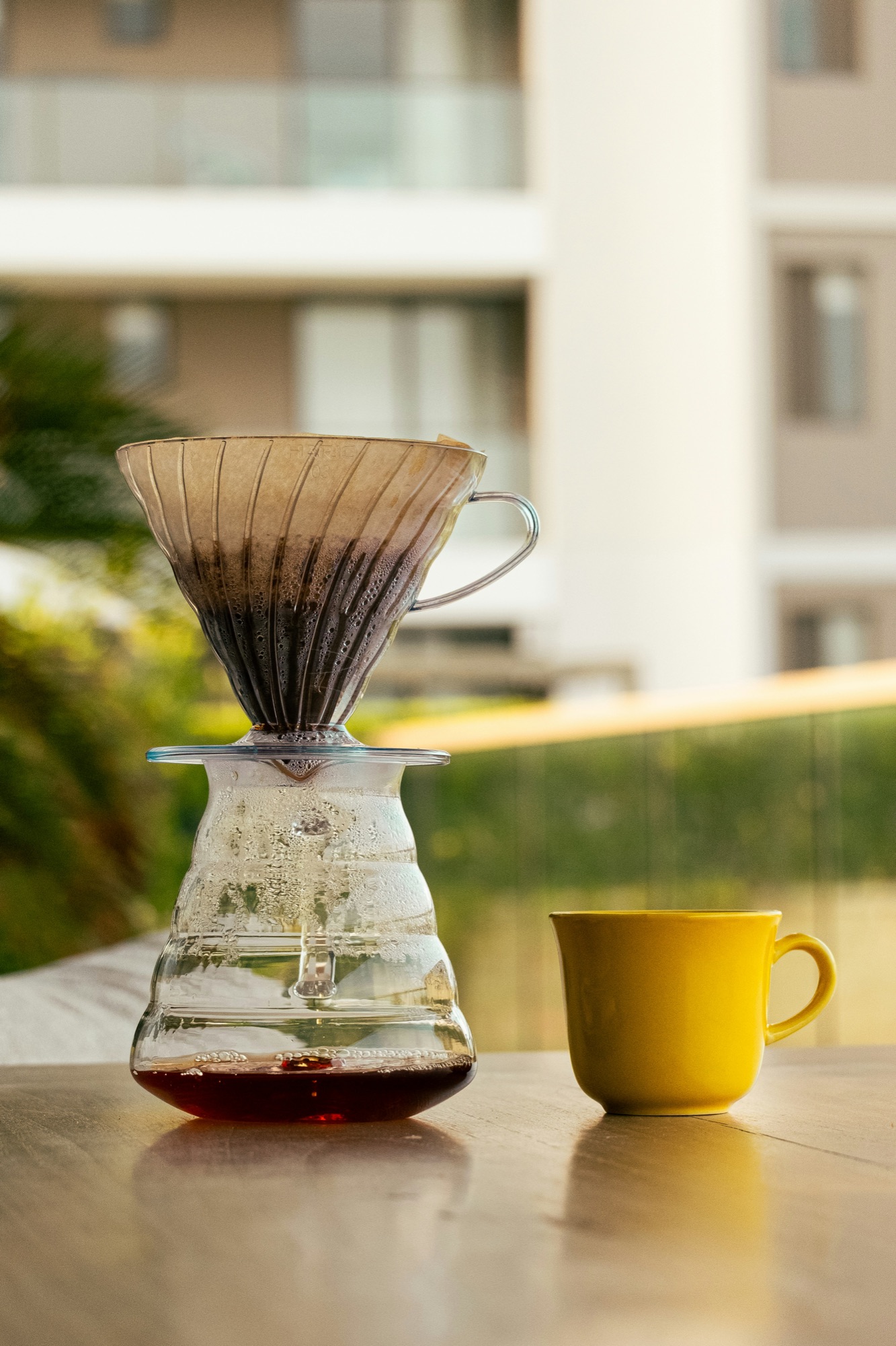 Café filtrado recién preparado junto a una taza amarilla al aire libre